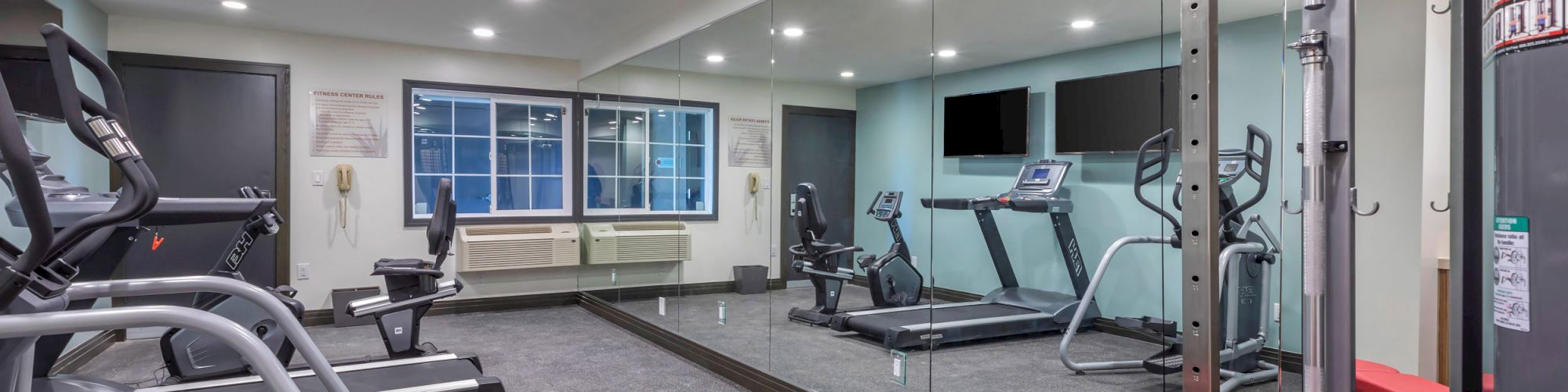 A modern indoor gym equipped with treadmills, elliptical machines, weight benches, and mirrored walls.