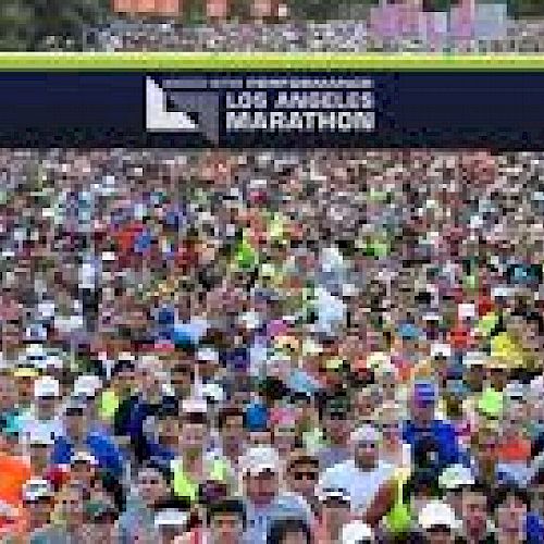 A large crowd of runners is gathered at the starting line for the Los Angeles Marathon, as indicated by the banner overhead, ready to start the race.