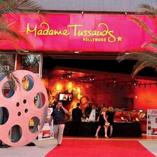 Picture of the entrance to Madame Tussauds in Hollywood, adorned with palm trees, large film reels, and a red carpet leading inside.
