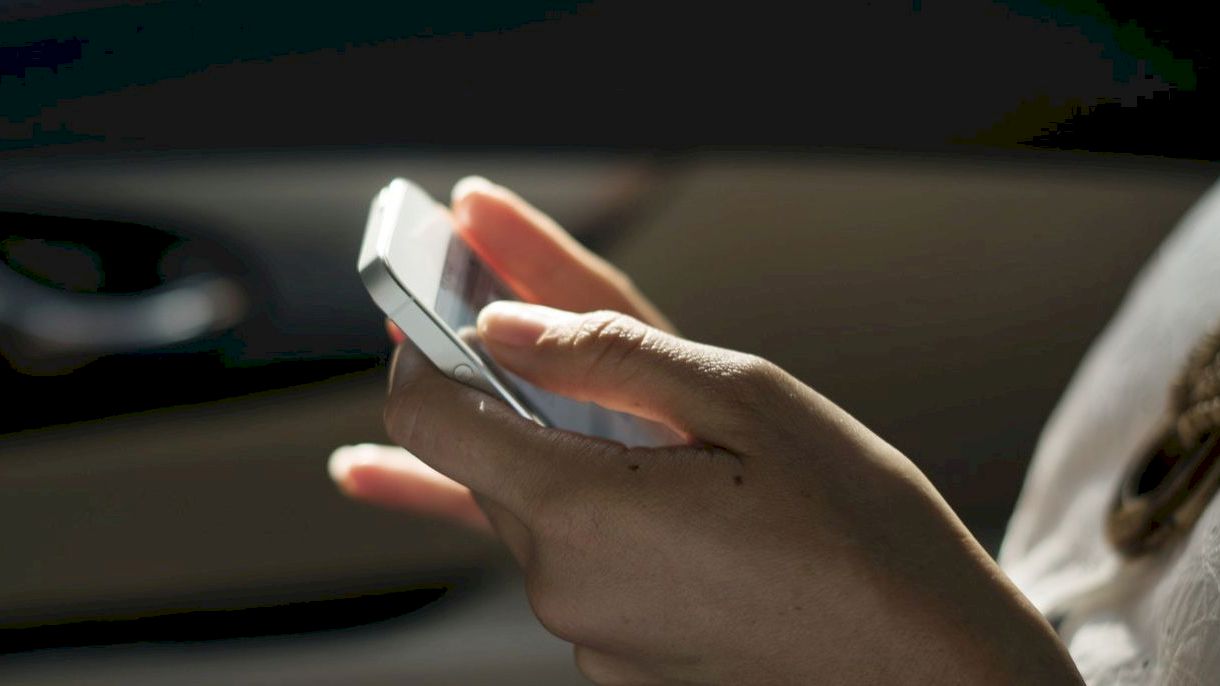 A person is holding and using a smartphone while sitting in a car. The focus is on the hands and the phone.