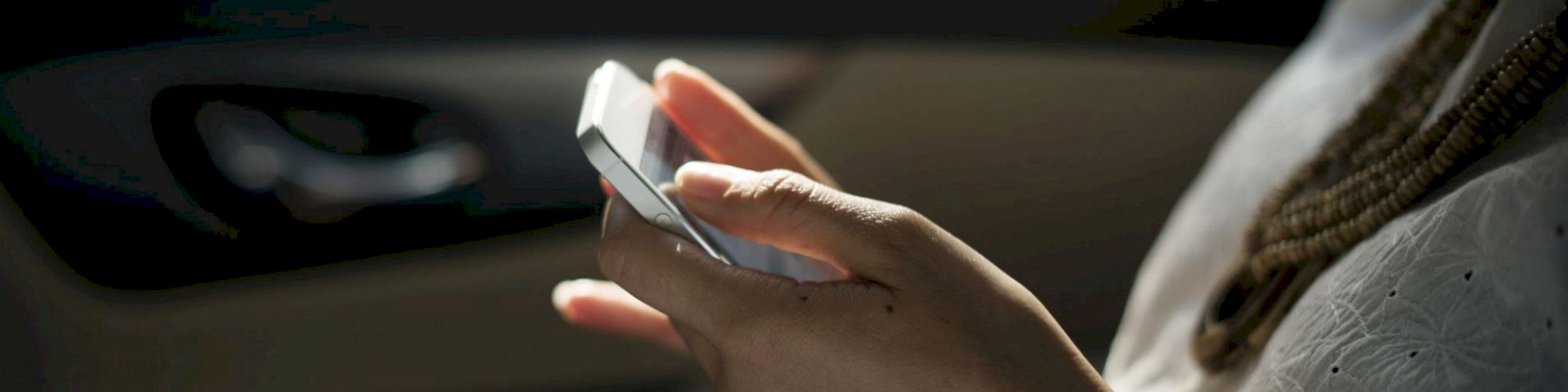 A person is holding and using a smartphone while sitting in a car. The focus is on the hands and the phone.