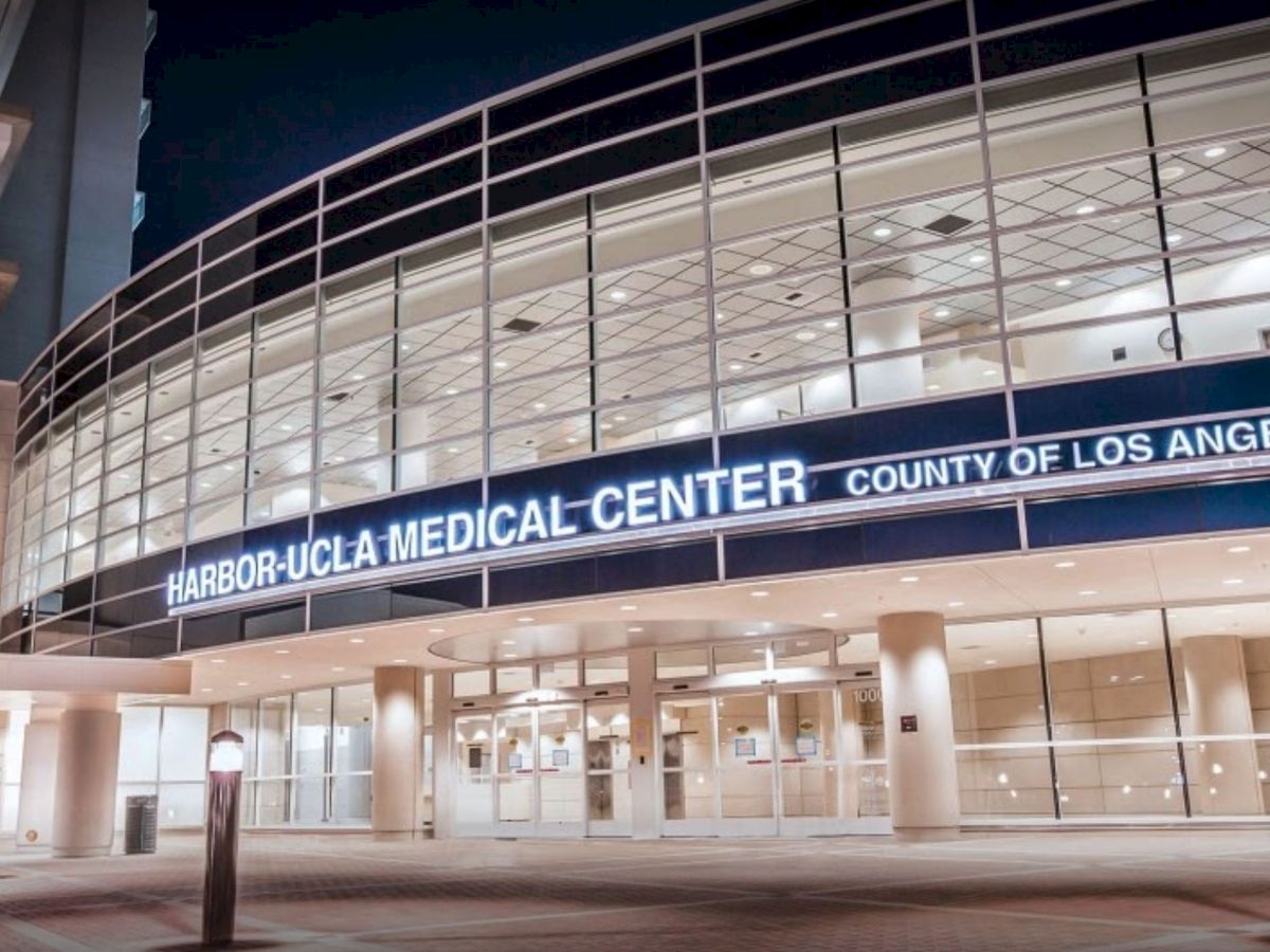 The image shows the entrance of Harbor-UCLA Medical Center, County of Los Angeles, with a glass facade and illuminated signage at night.