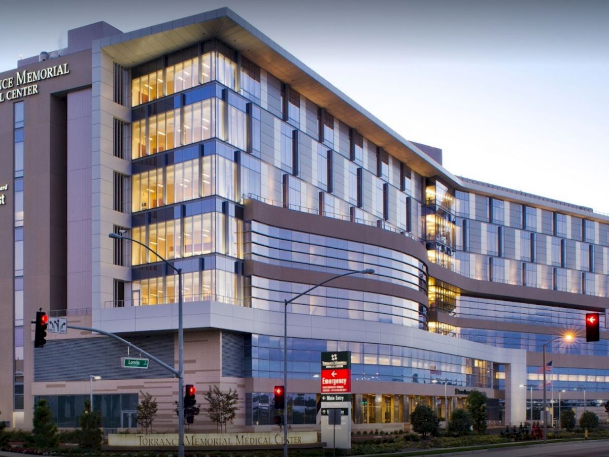 A modern multi-story building identified as Torrance Memorial Medical Center, Lundquist Tower, with lighted windows and situated at a street intersection.