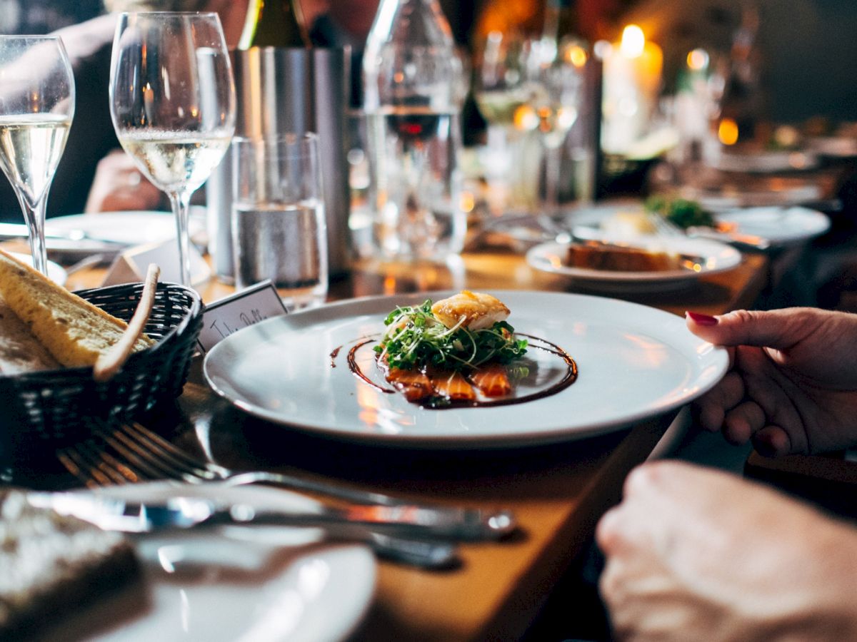 A fine dining setup with a focus on a dish of gourmet food, glasses of wine, and a basket of bread on a beautifully arranged table.