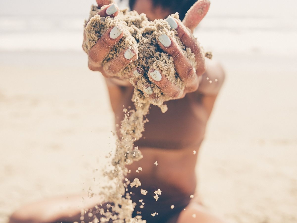 A person sitting on a beach, holding and letting sand fall through their hands.