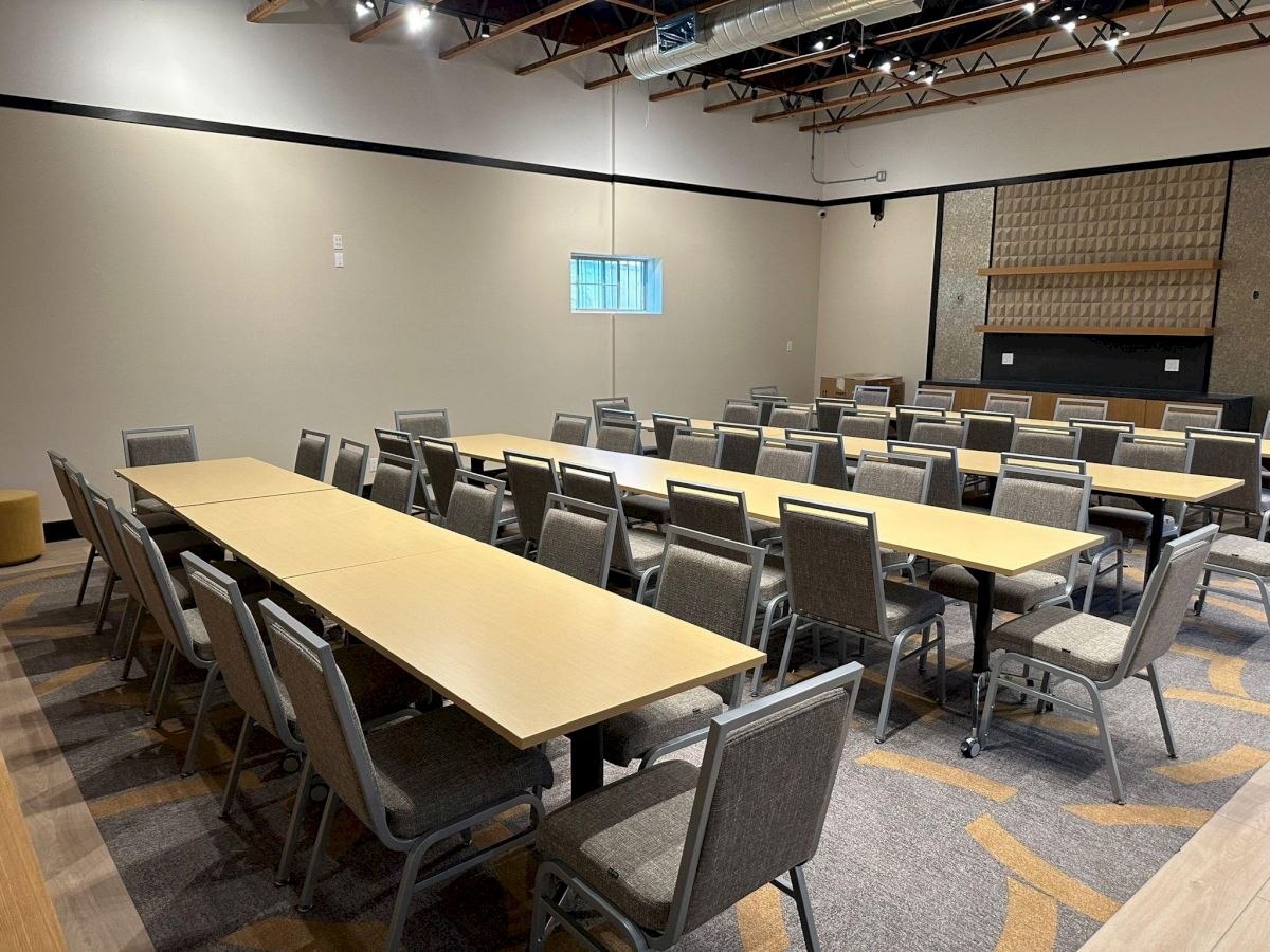 A conference room setup with rectangular tables and around twenty-five chairs, arranged in rows facing a front wall.