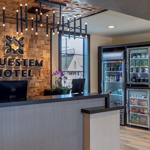 This image shows the front desk area of the Bluestem Hotel, featuring a modern design with a wooden accent wall and a convenience store section.