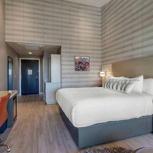 A modern hotel room featuring a large bed, desk with chair, wall-mounted TV, and stylish decor in neutral tones.