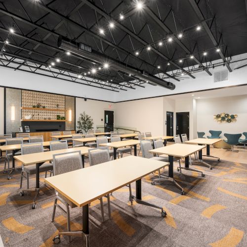 The image shows a modern conference room with tables, chairs, plants, and ceiling lights in a bright and spacious setting.