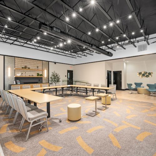 A modern conference room with a U-shaped table, seating, decorative plants, and overhead lighting fixtures.