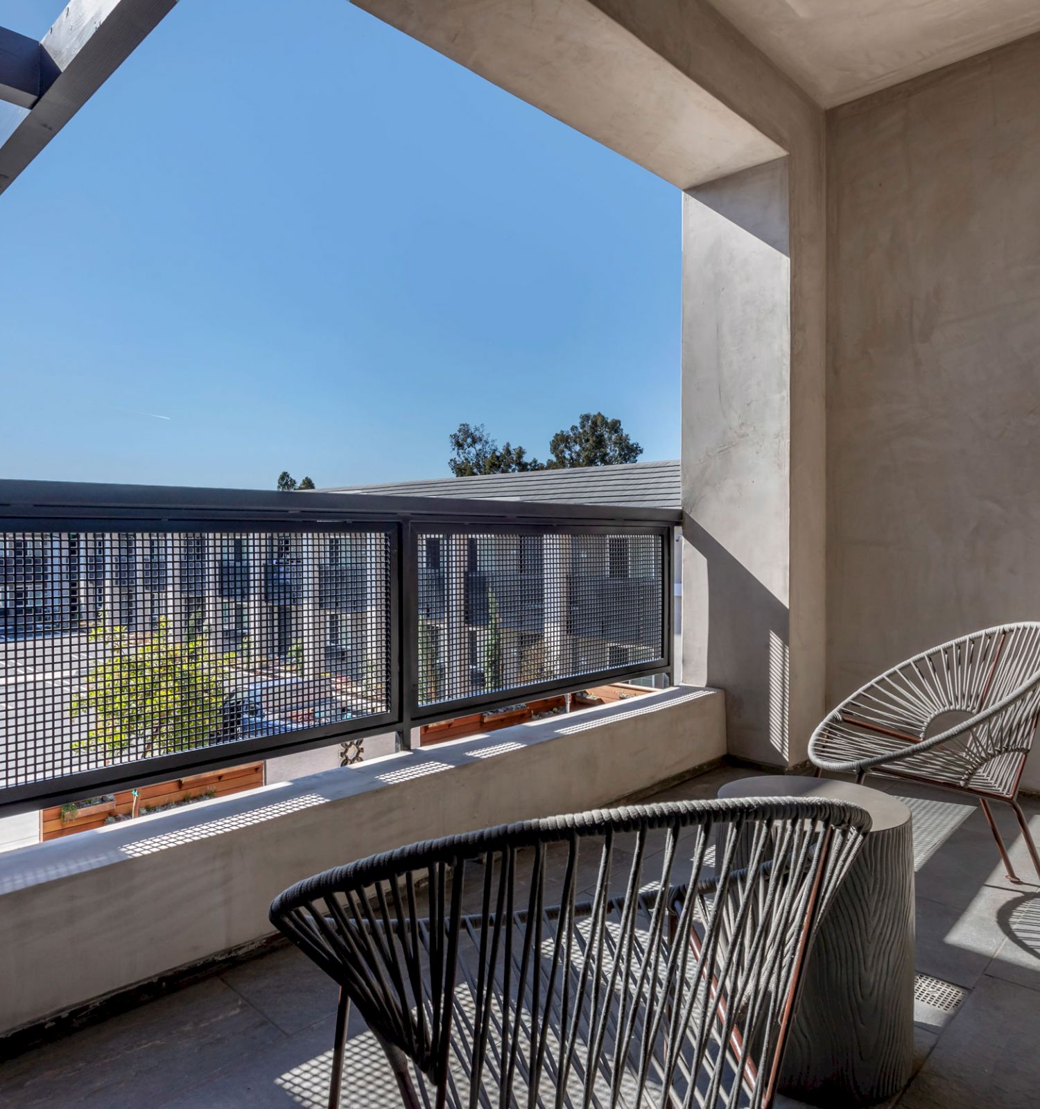 A modern balcony with two contemporary chairs, a small table, and a clear view of a sunny blue sky and nearby buildings.