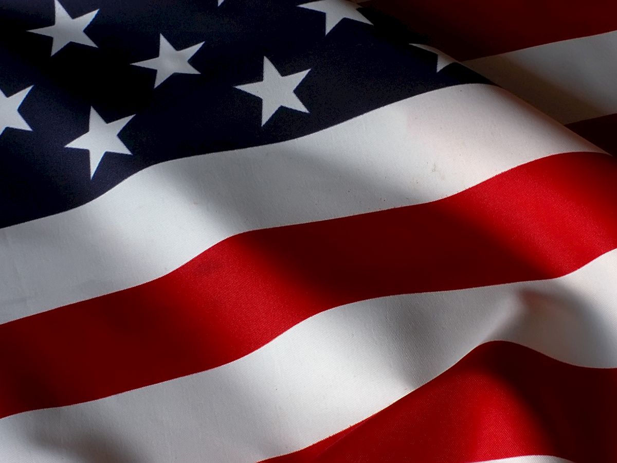 The image shows a close-up of the United States flag, featuring stars and stripes in red, white, and blue colors.