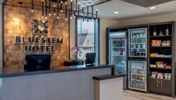 This image features the reception area of Bluestem Hotel with a front desk, modern lighting, and a display of various snacks and beverages.