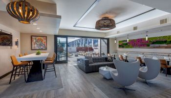 A modern living area with stylish furniture, a dining table, and an outdoor patio. Natural light fills the space from large windows and skylights.