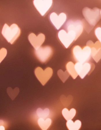 The image shows a bokeh effect with heart-shaped lights in soft pink and orange tones against a blurred background.