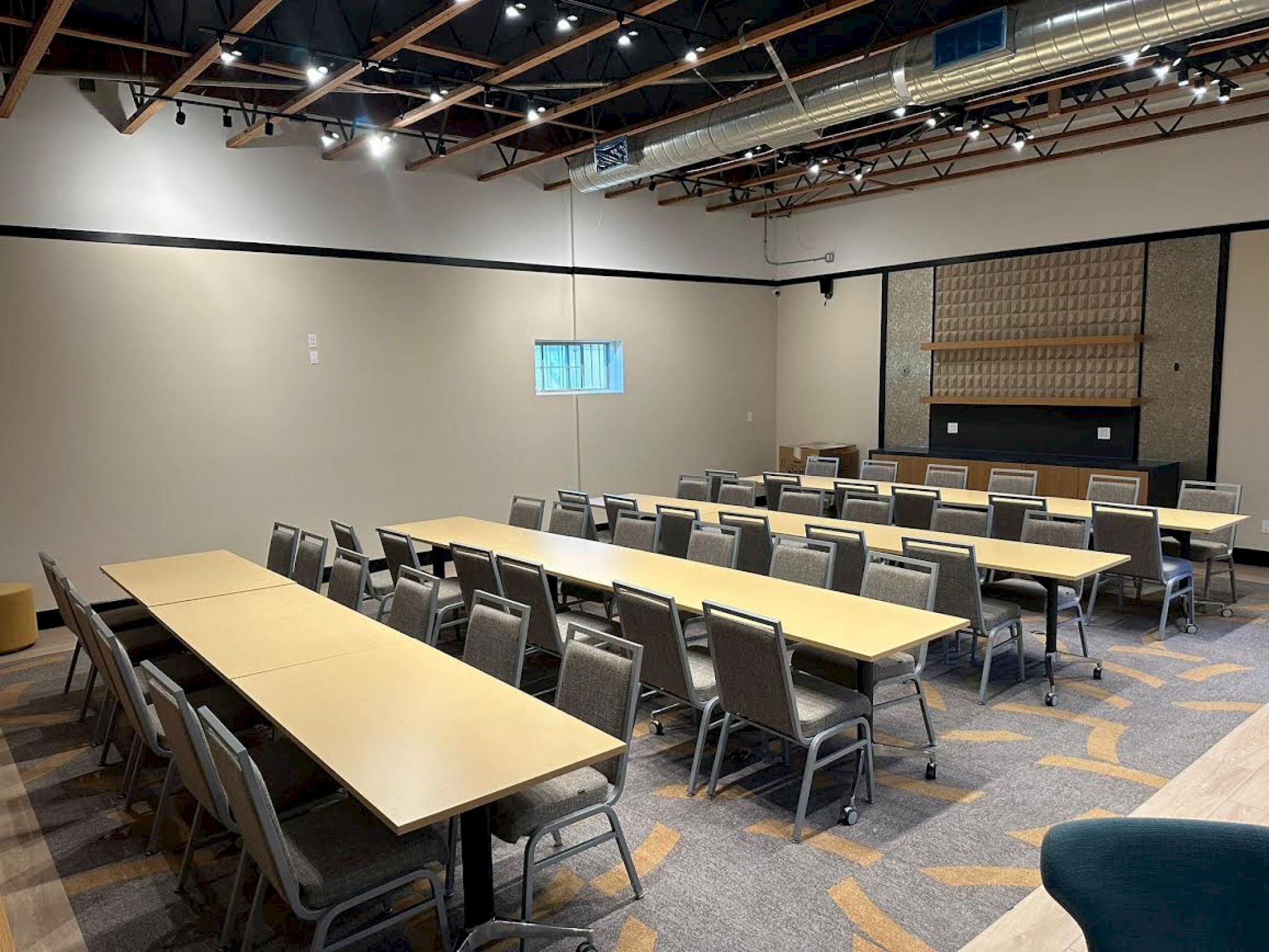 The image shows an empty conference room with rows of tables and chairs set up for a meeting or event, under a well-lit ceiling.