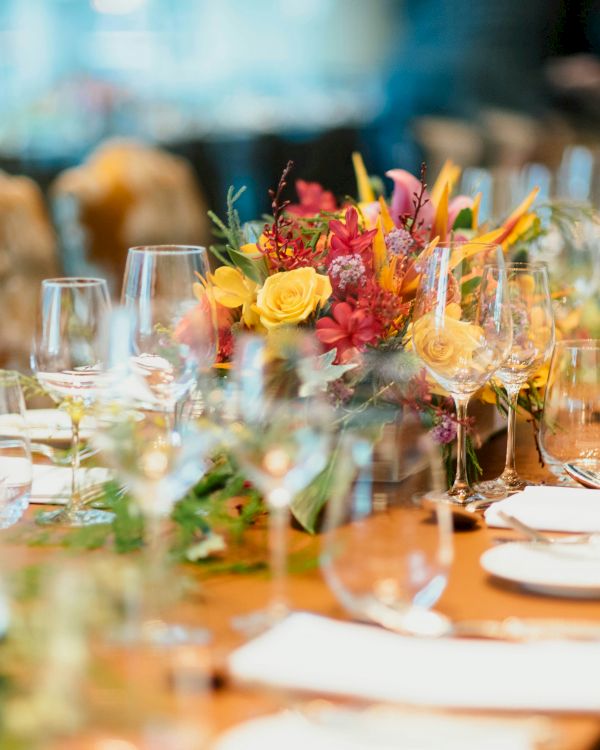 A beautifully set, elegant table with glassware, plates, cutlery, and a vibrant floral centerpiece, ready for a formal gathering or event.