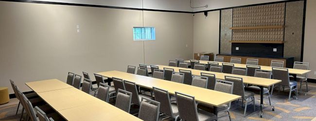 The image shows a conference room set up with long tables and chairs arranged for a meeting or event. The ceiling has exposed beams.