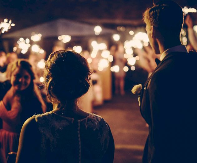 A couple stands facing a crowd holding sparklers at a nighttime celebration or event, creating a festive and joyful atmosphere.