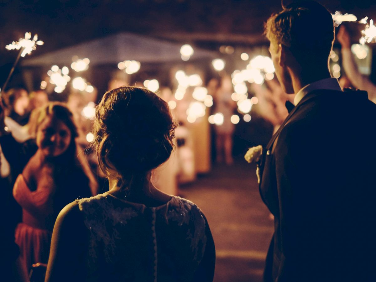 A couple stands as guests hold sparklers, creating a festive and warm atmosphere in a dimly lit outdoor setting.