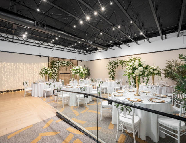 An elegantly decorated banquet hall with round tables, white chairs, floral centerpieces, and string lights on the walls.