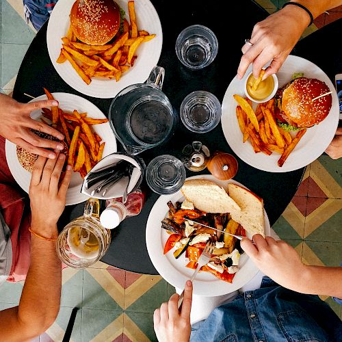 Three people seated around a table enjoying burgers, fries, and another dish in a lively setting with patterned flooring.